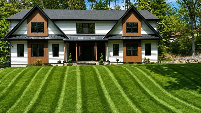 Modern farmhouse with white and wood exterior, black roof, dual gables, and manicured lawn with diagonal stripe pattern