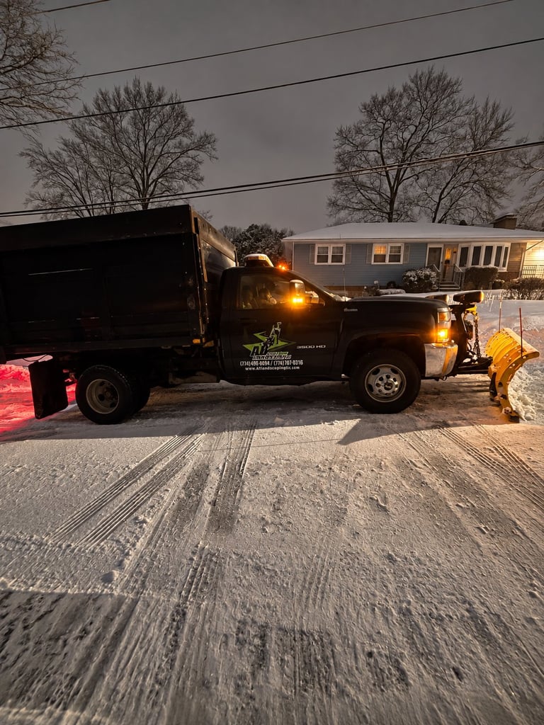 Black dump truck with yellow lights parked on snowy driveway in front of residential house at dusk